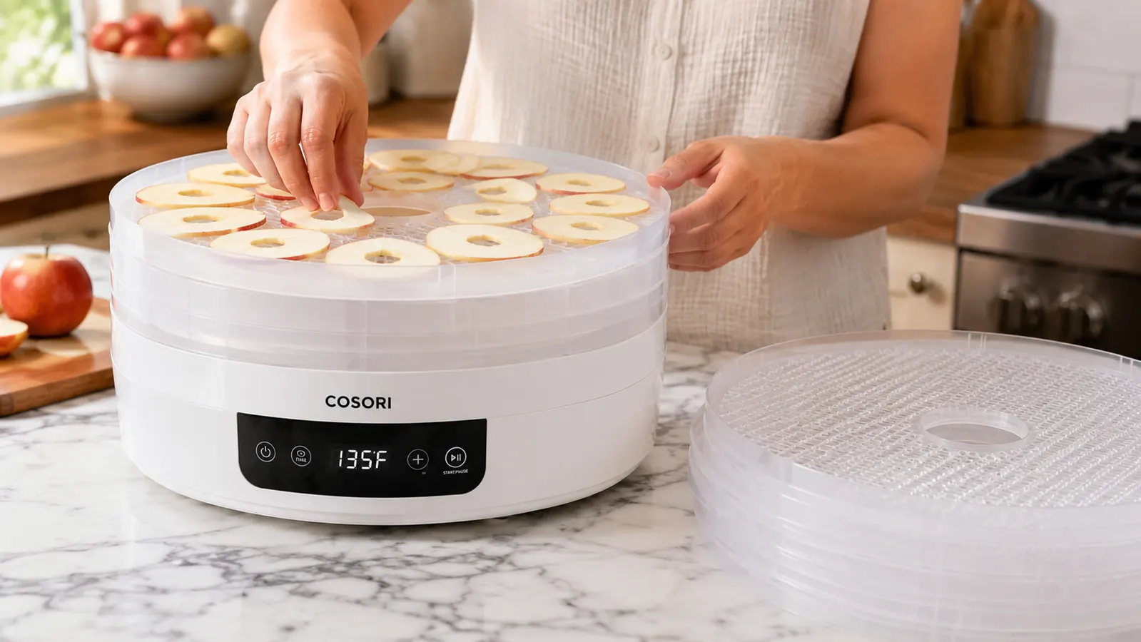 Hand loading sliced apple rings onto a mesh tray of the Cosori Food Dehydrator
