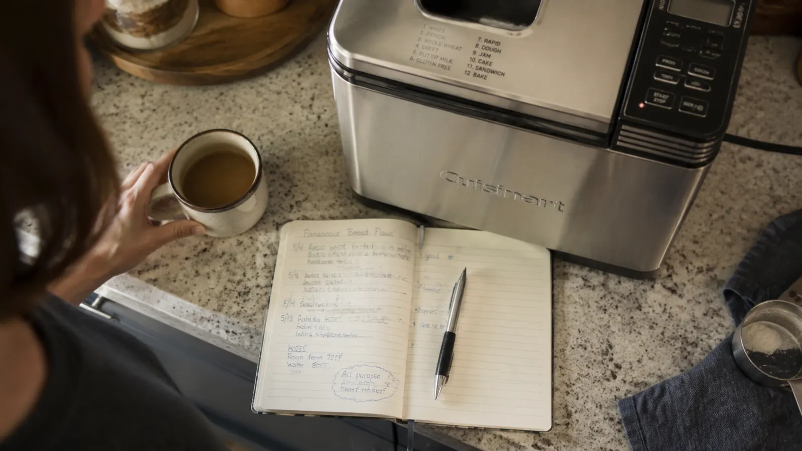 Cuisinart Bread Maker sitting quiet on a counter next to a spreadsheet notebook tracking loaf results
