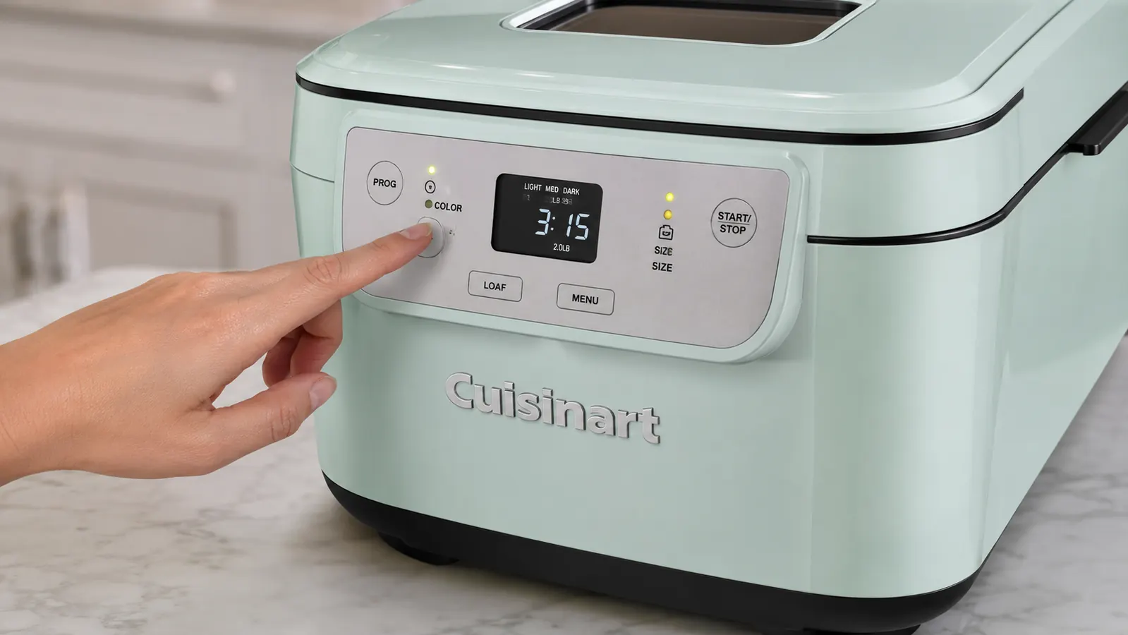 Hand pressing the digital control panel on the Cuisinart bread maker to start the whole wheat cycle