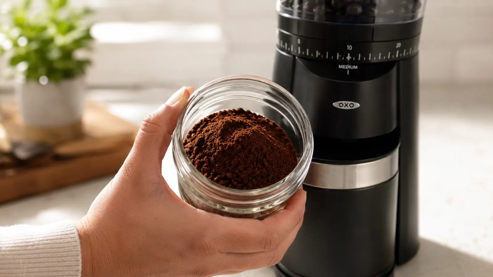 A hand tilting the OXO grinder's ground coffee container to show a light dusting of static-clung grounds along the inside edge