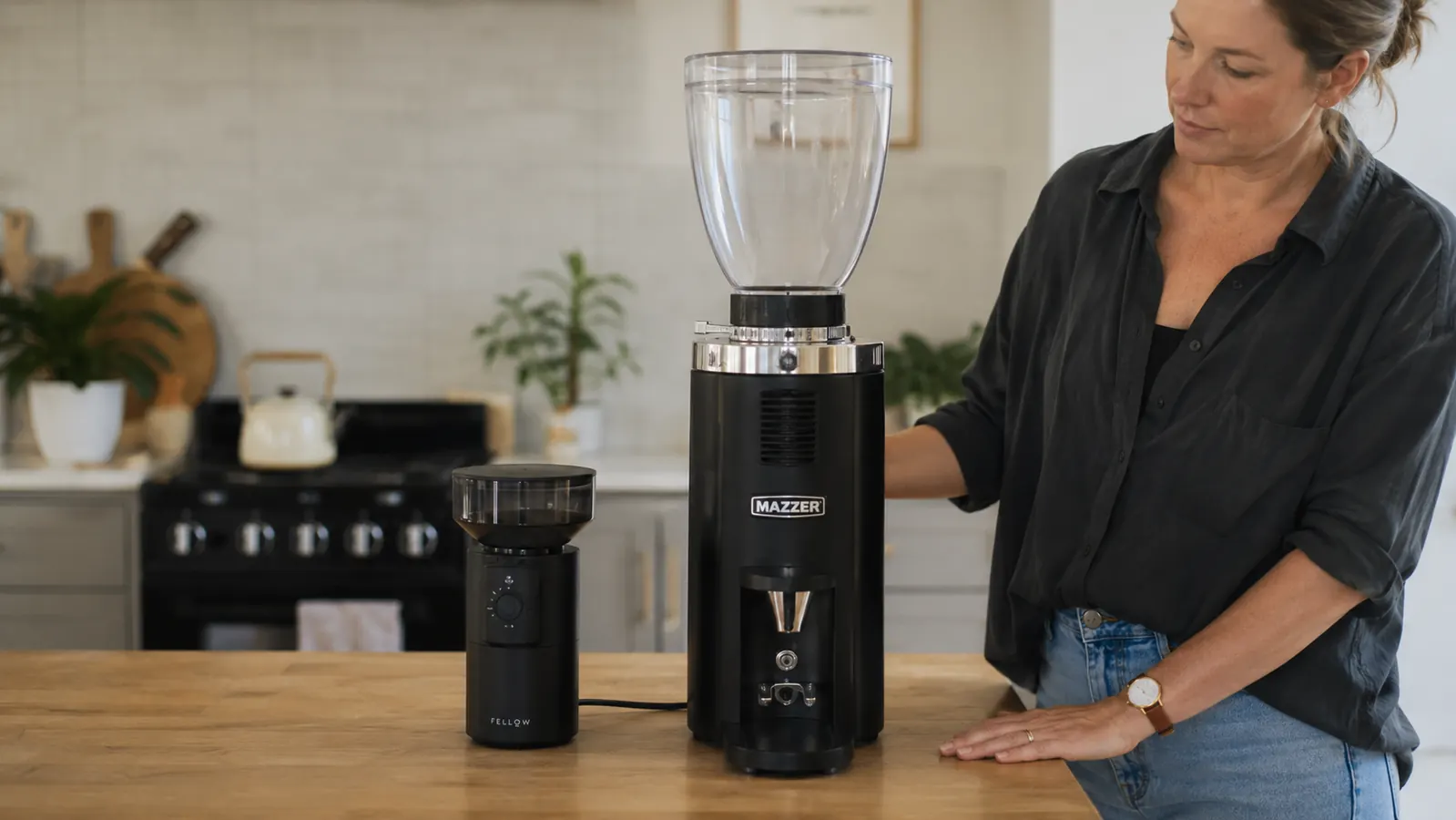 Two burr coffee grinders, one matte black and one with a clear bean hopper, sitting side by side on a kitchen counter