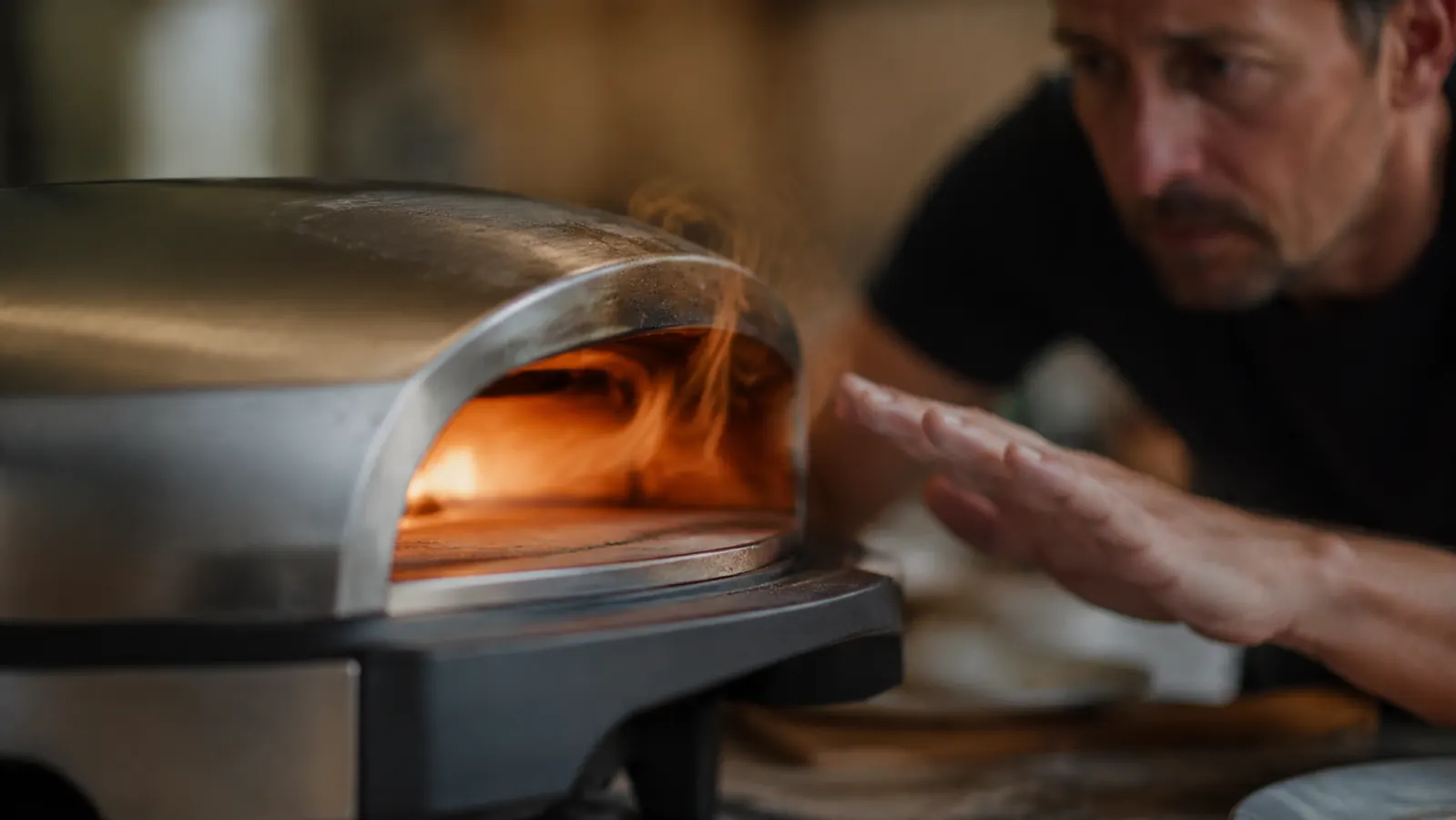 Close-up of a hand hovering near the PIEZANO oven's exterior housing with visible heat shimmer, illustrating how hot the outer shell gets during a bake